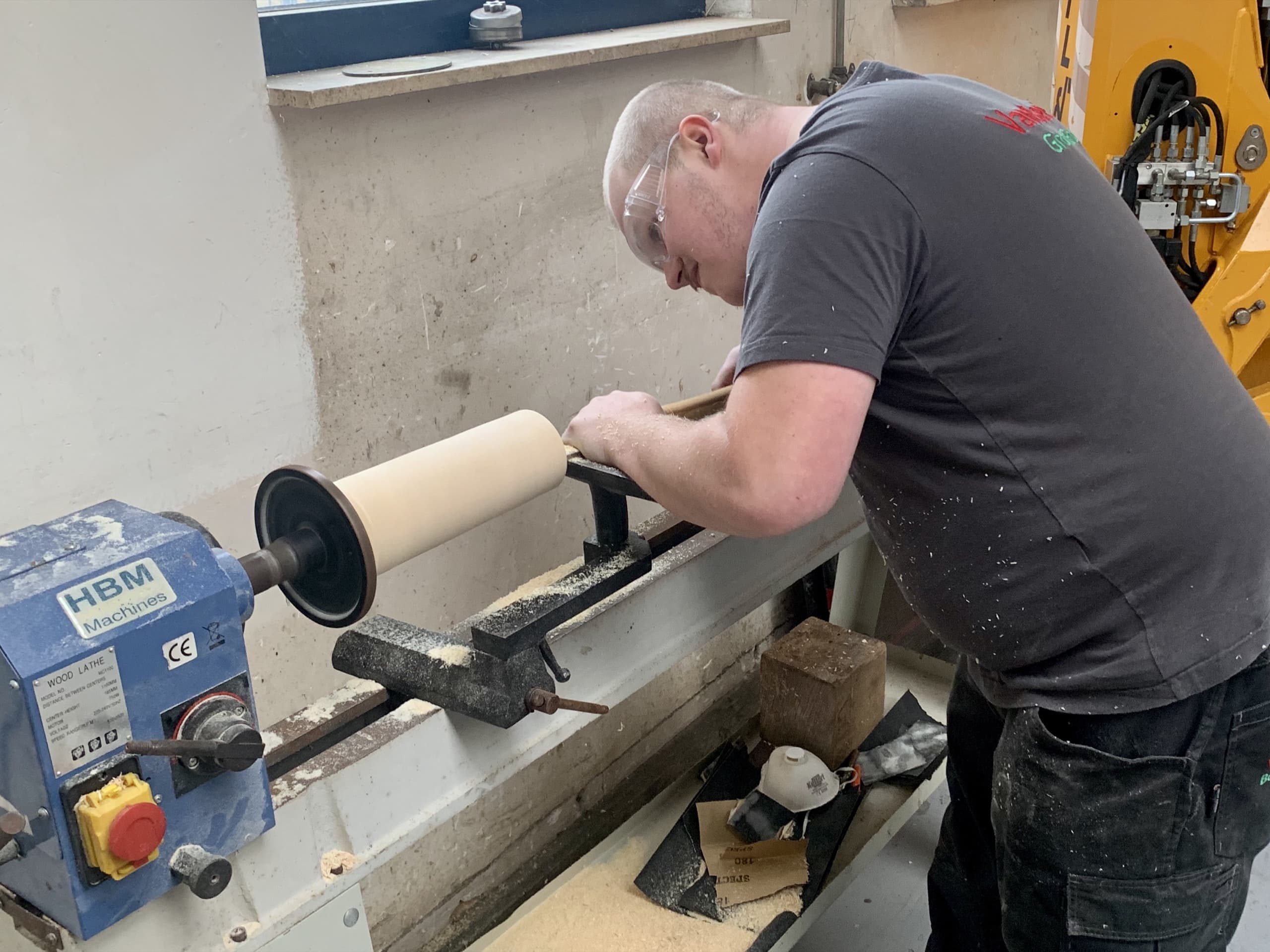 Een deelnemer aan dagbesteding bij Stichting Van Beets werkt aan een houtdraaibank in de werkplaats, met een blok hout en schuurpapier binnen handbereik.