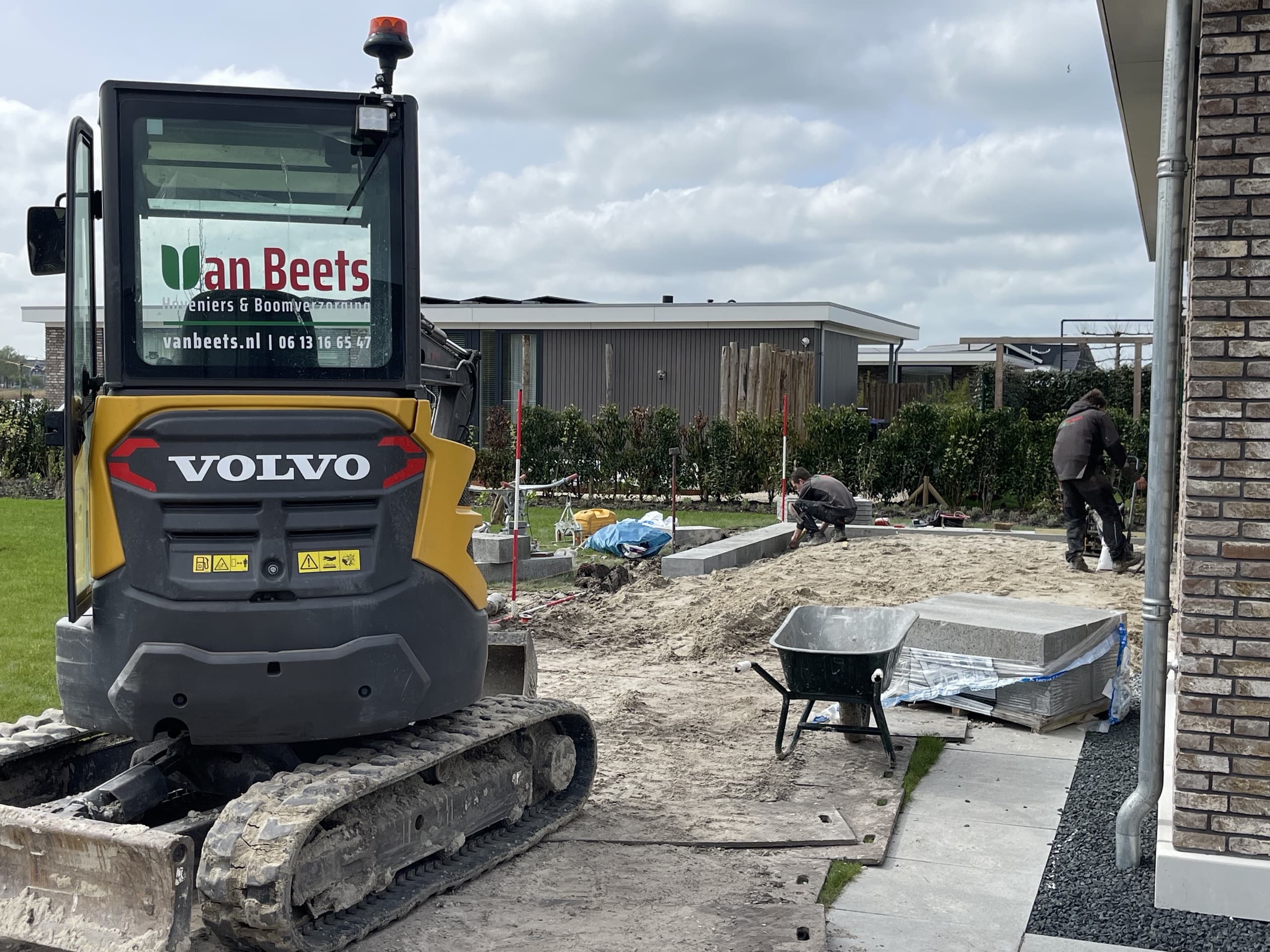 Collega's van Van Beets leggen een terras aan bij een nieuwbouwwoning in Leeuwarden, met op de voorgrond een mini-graafmachine en een kruiwagen.